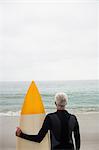 Rear view of senior man in wetsuit holding a surfboard