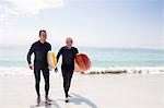Happy father and son in wetsuit walking with surfboard