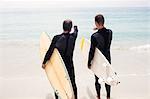 Rear view of father and son standing with surfboard and pointing at a distance