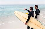 Father and son standing with surfboard and pointing at a distance