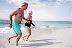 Senior couple holding hands and running on the beach