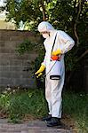 Man in protective workwear while spraying pesticide on grass