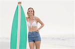 Pretty blonde woman standing next to a surfboard