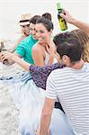 Group of friends sitting on the sand having a beer