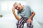 Frustrated senior man on bed at home