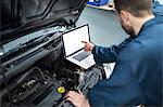 Mechanics examining car engine using laptop