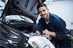 Mechanic smiling at camera while examining car engine