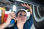 Female mechanic examining car using flashlight