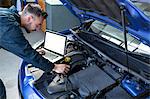 Mechanic examining car engine with help of laptop