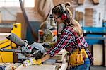 Female carpenter cutting wooden plank with electric saw