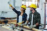 Male and female carpenter looking up and pointing while working