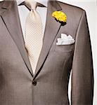 Detail of a light brown suit jacket with cream colored shirt and white handkerchief, yellow patterned necktie and yellow flower