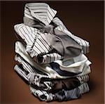 Stack of men's, striped dress shirts with ties on brown background