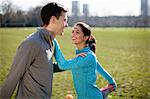 Young woman and man doing warm up stretch training in park