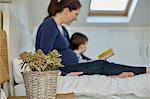 Side view of pregnant mother and baby boy sitting on bed reading book together