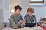 Boys in pyjamas using digital tablet in bed