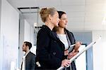 Businesswomen with blueprint and digital tablet inspecting in new office