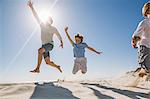 Father and sons on beach, arms raised jumping in mid air