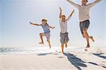 Father and sons on beach, arms raised jumping in mid air