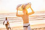 Boy on beach carrying surfboard over head