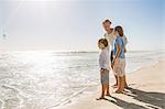 Full length side view of father and sons on beach looking away at ocean