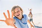 Boy on beach looking at camera, hand raised smiling