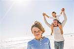 Father and sons on beach, carrying on shoulders smiling