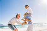 Big brother on beach carrying brother on shoulders, father tickling