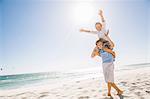 Full length view of big brother on beach carrying brother on shoulders, arms raised smiling