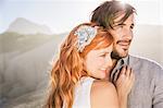 Man hugging red haired woman in front of rocks looking away smiling