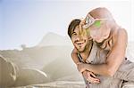Man in front of rocks giving woman piggyback smiling