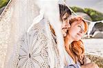 Couple on beach sitting in lace teepee looking away