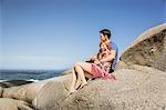 Couple sitting together on rocks, looking at ocean