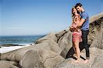 Couple standing on rocks beside ocean, hugging