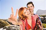 Portrait of couple outdoors, young woman making peace sign, smiling