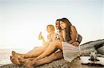 Three mid adult friends sitting on beach with bottled beer at sunset, Cape Town, South Africa