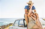 Mid adult couple sitting on top of car on coast road, Cape Town, South Africa