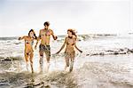 Three adult friends wearing bikini's and swimming shorts running in sea, Cape Town, South Africa