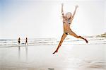 Mid adult woman wearing bikini jumping mid air at beach, Cape Town, South Africa