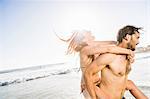 Mid adult man giving girlfriend piggyback on sunlit beach, Cape Town, South Africa