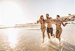 Three mid adult friends running in sea, Cape Town, South Africa