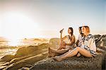 Three mid adults sitting on beach looking out at sunset, Cape Town, South Africa