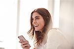 Happy young woman using smartphone in front of window