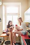 Two young woman sitting on kitchen counter chatting