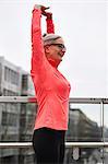 Mature woman training in city, stretching arms on footbridge