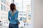 Rear view of young woman listening to music looking through city apartment window