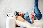 Young woman lying on sofa with legs raised reading a book