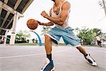 Cropped view of man on basketball court running, bouncing basketball