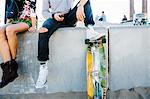 Young couple sitting on wall, man resting foot on skateboard, low section