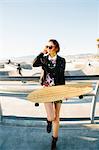 Young woman standing by railings, near skate park, holding skateboard